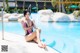 A woman in a bikini sitting on the edge of a swimming pool.