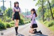 Two young women in school uniforms holding hands on a road.