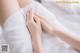 A woman in a white dress laying on a bed with her hands on her knees.