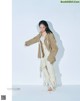 A woman in a beige jacket and white pants posing for a magazine.