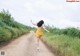 A woman in a yellow dress running down a dirt road.