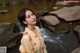 A woman in a yellow kimono standing in front of a waterfall.